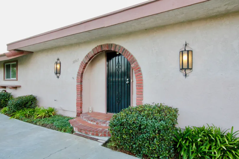 Beige stucco residence with brick archway over the entrance and flanking laterns in Montecito Plaza of Garden Grove, CA