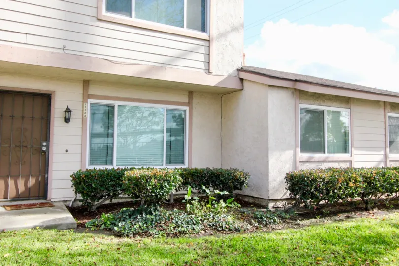 THE FRONT OF THE VILLA WITH GLASS WINDOWS, LAWN, SMALL CROTONS ARE PLANTED IN GARDEN GROVE CITY