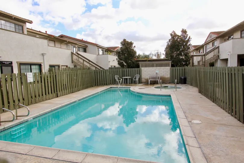 A clean pool decorated with chairs inside the compound wall near building decorated with trees and plants in Spring Garden Villas