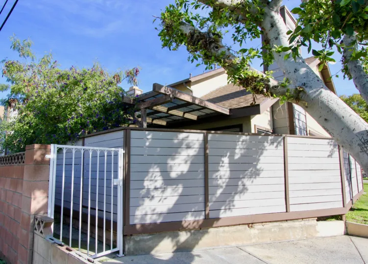 THIS IMAGE VIEWS THE GATEWAY TO THE HOUSE THAT HAS THE TREES, PLANTS, AND SURROUNDED THE WALL GATES IS PLACED IN THE COMMUNITY OF STANFORD PLAZA