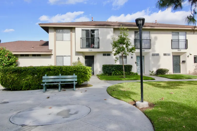 A sunny day showing the front of a multi room building and a green bench in the Westbrook community of Garden Grove California.