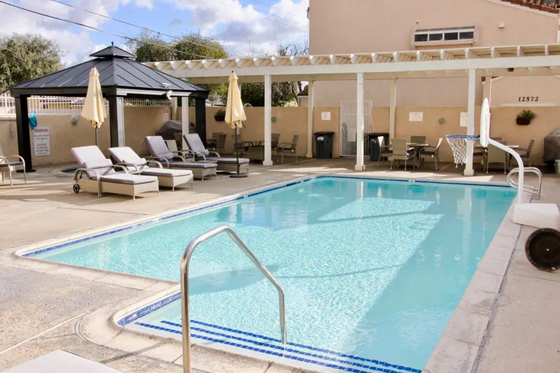THIS IMAGE REPRESENTS THE BEAUTIFUL SWIMMINGPOOL IS IN THE GARDEN GROVE THAT HAS THE LOT OF CHAIRS, TABLES AND NUMBER BOARD