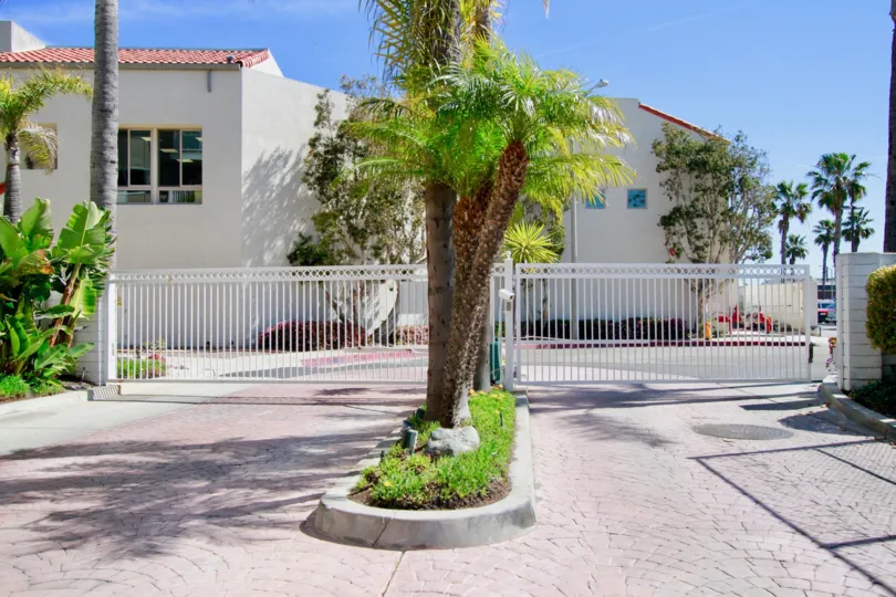 THE TREE LOCATED AT THE FRONT AND THE GATE NEXT TO THE TREES AND A BUILDING RED ROOF WITH WHITE COLOUR WALL AVAILABLE AT THE NEXT OF THE ENTRANCE GATE.