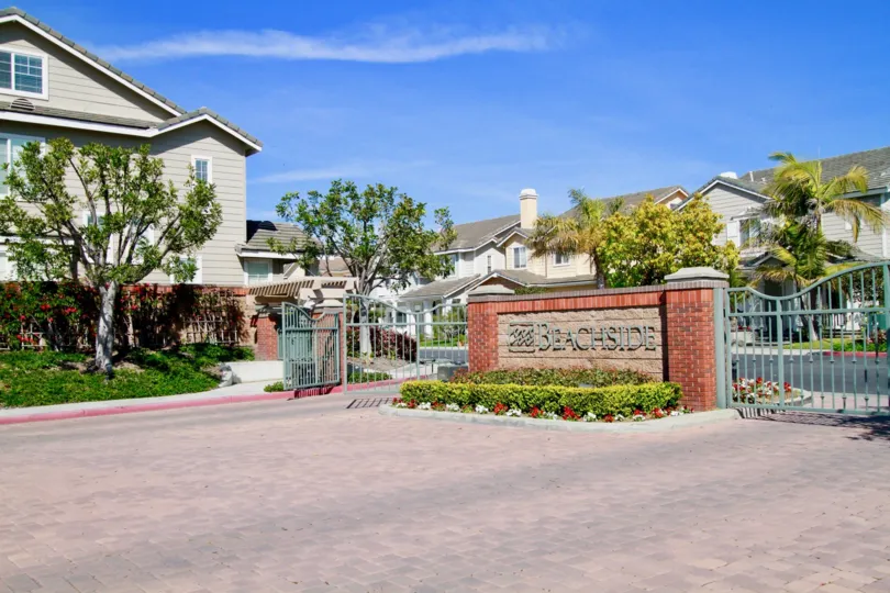 Beachside community entrance with gates and trees on a sunny day.