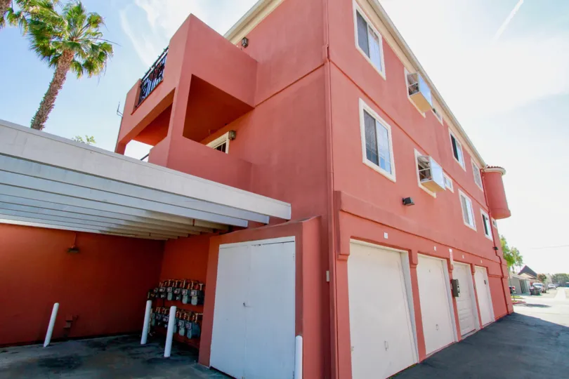 THE BUILDING WITH MILD RED COLOUR AND THREE SMALL PILLARS NEAR OF THE HOUSE A BALCONY WITH A SIGN BOARD AVAILABLE.