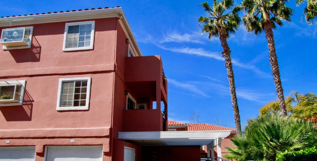 A BUILDING WITH MAROON COLOUR AND MORE WINDOWS AND AC COOLORE AVAILABLE AT THE FLOOR A BALCONY ALSO AVAILABLE AND SOME TREES IN FRONT OF THE BUILDING