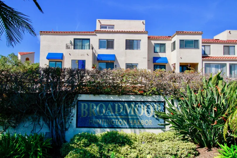 Broadmoor Huntington Harbor sign with bushes and cacti on a sunny day.