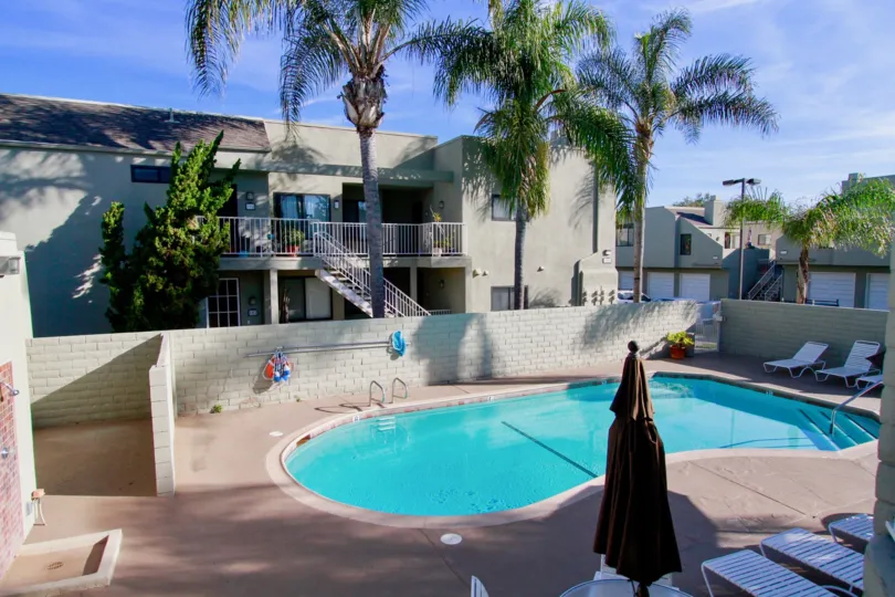BrookstoneHuntington Beach California bulding center place round shape swmming pool blue color water near to stepesback side three palm tree and balcony and steps same home color light gray