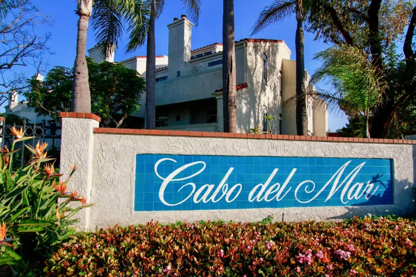 THE BOARD OF SIGN REPRESENTS CABO DEL MAR AND MORE FLOWERS ARE IN FRONT OF THE BOARD AND A BUILDING BACKSIDE OF THE SIGN AND SOME TREES ALSO AVAILABLE.