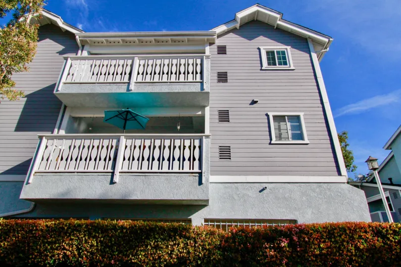 A three story town home with large balcony towers above a green hedge inside Capewoods in Huntington Beach CA