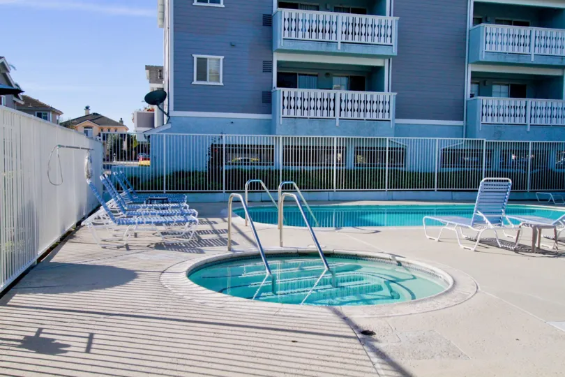 Capewoods pool and hot tub with a fence and deck chairs on a sunny day.