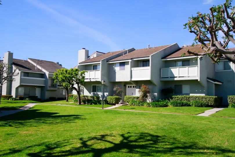The white color buildings in the Cherrywood Village with glass windows, big trees, green grass and ornamental shrubs.