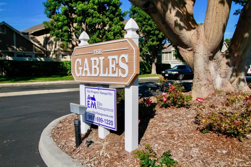 Gables sign with a lamp and a trees around it on a sunny day.