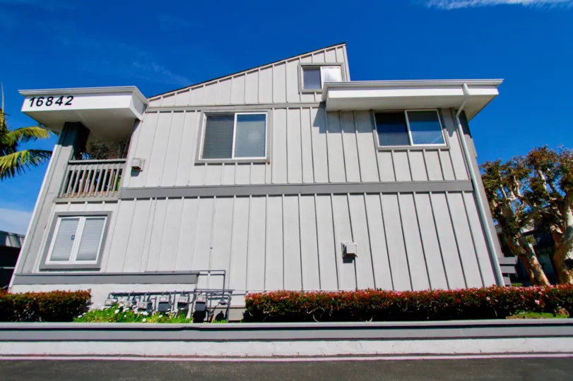 A Harboring Villas building with gray siding and bushes on a sunny day.