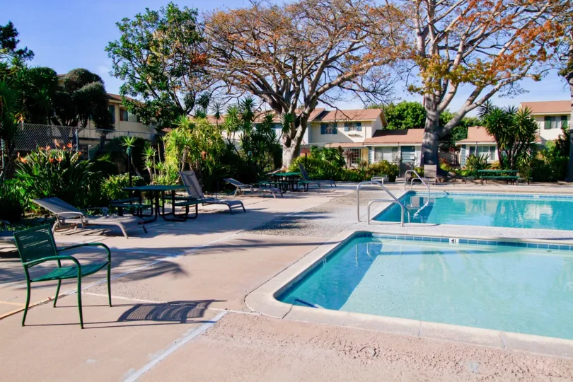 A sunny day in the Huntington Bay with swimming pool, chairs, tables and also with trees and plants.