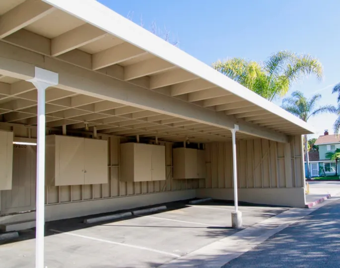 THE PLACE LOOKS LIKE A PARKING STAND WITH WHITE COLOUR AND A TREE NEAR TO THE STAND AND TWO PILLARS AVAILABLE AT THE PLACE