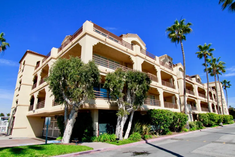 Huntington Harbour Bay Club apartments with balconies and palm trees on a sunny day.