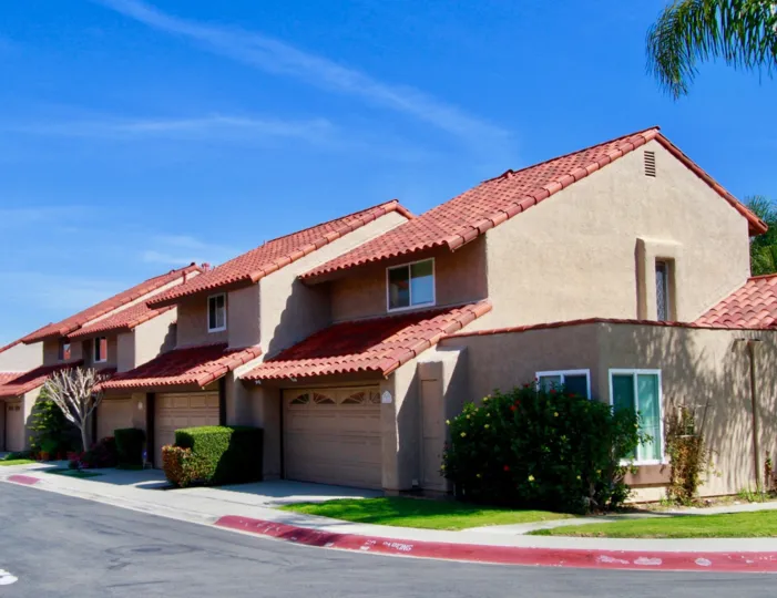 The buildings in the La Cuesta Racquet Club with green grass, ornamental flowering plants near the road side.