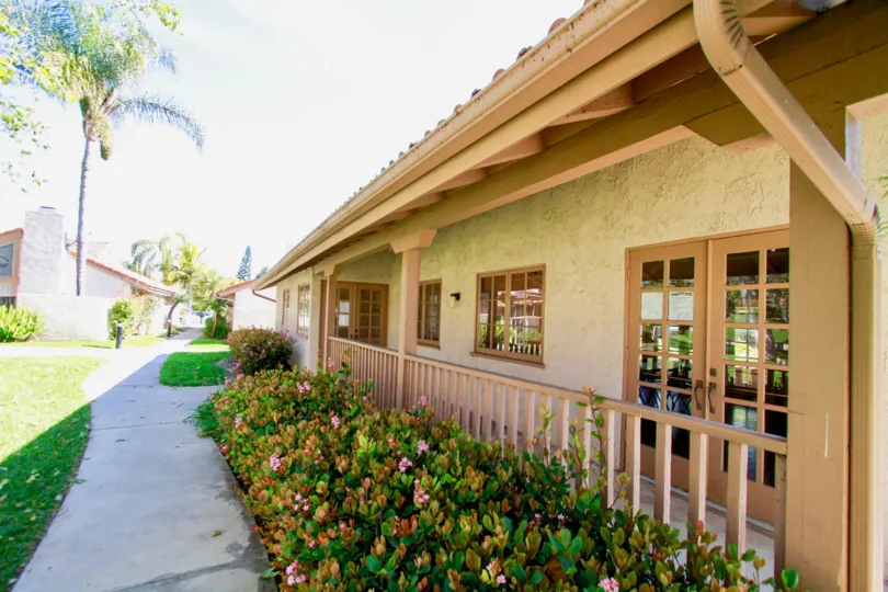 La Cuesta Tennis Club building with bushes and a sidewalk on a sunny day.