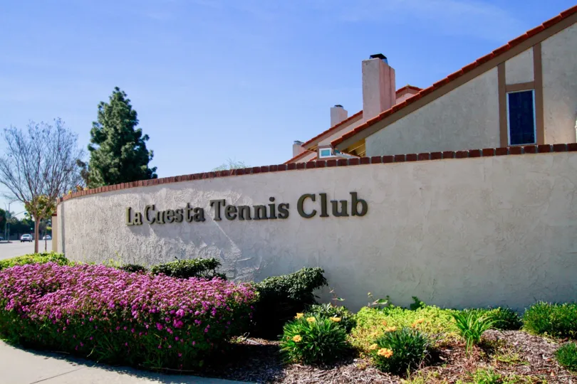 La Cuesta Tennis Club sign with flowers and bushes on a sunny day.