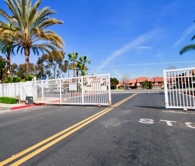 Metal gate to Las Brisas with palm trees on either side on a sunny day.