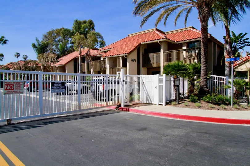 THE GATE WITH A NO PARKING BOARD AND A ROAD IN FRONT OF THE GATE A HOUSE INSIDE THE ENTRANCE WITH A BEAUTIFUL CAR.
