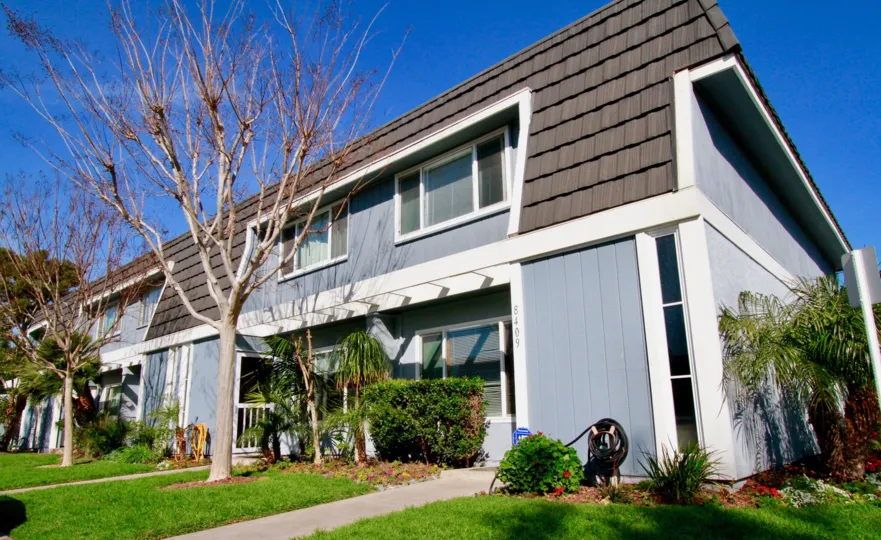 Mariners Cove apartments with trees and a hose on a sunny day.