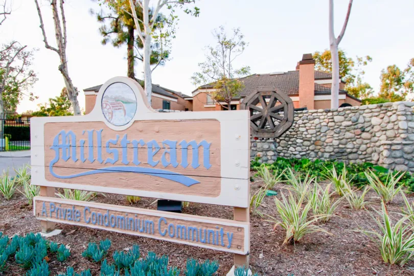 Millstream sign with plants and a stone fence on a cloudy day.