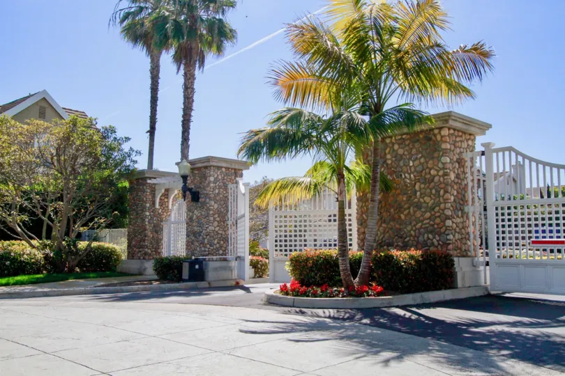 Mystic Pointe gate with palm trees and flowers on a sunny day.