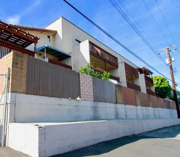 THE BUILDING COVERED WITH FULL ENTRANCE WALL AND THE POST LINE NEAR TO THE HOUSE SOME TREES ALSO INSIDE THE WALL AND SKY LOOKING SUNSHINE TIME.