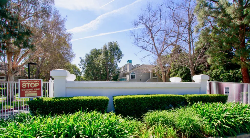 Pacific Ranch Villas entrance with a metal gate and bushes on a sunny day.