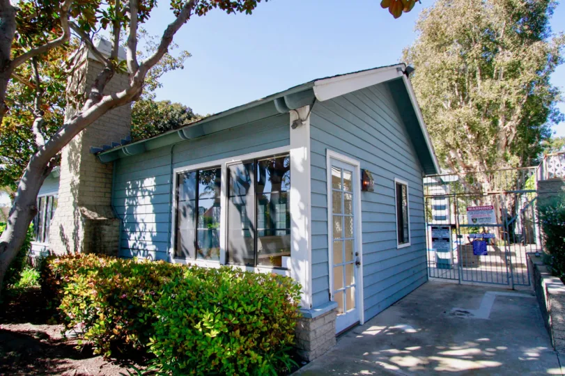 A beautiful house with glass windows in the Pelican Cove with ornamental flowering plants and big trees.