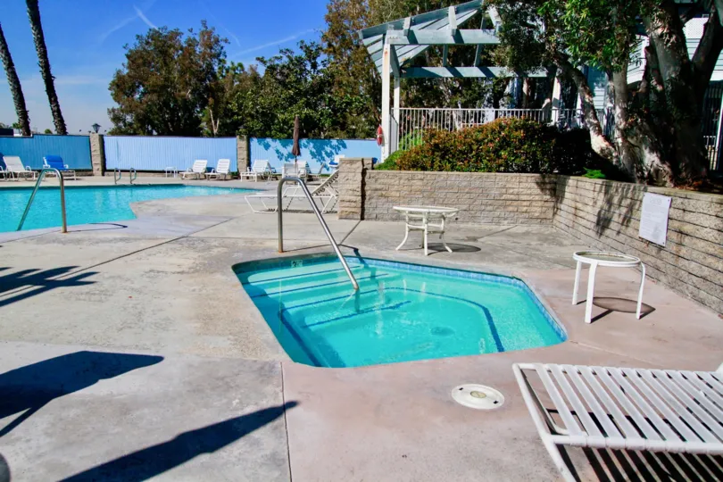 Pelican Cove pool and hot tub with a fence surrounding them on a sunny day.