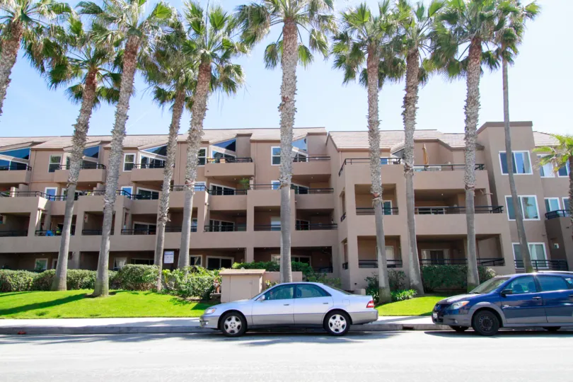 THE APARTMENT LOOKING SO LARGE AND IN FRONT OF BEAUTIFUL GARDEN AVAILABLE MORE TREES ALSO THERE AND TWO CARS PARKING IN FRONT OF THERE.