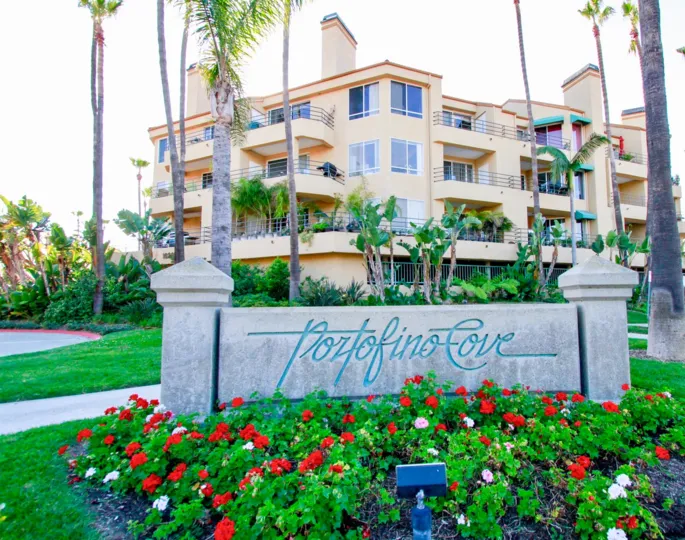 Portofino Cove sign with flowers and palm trees on a sunny day.