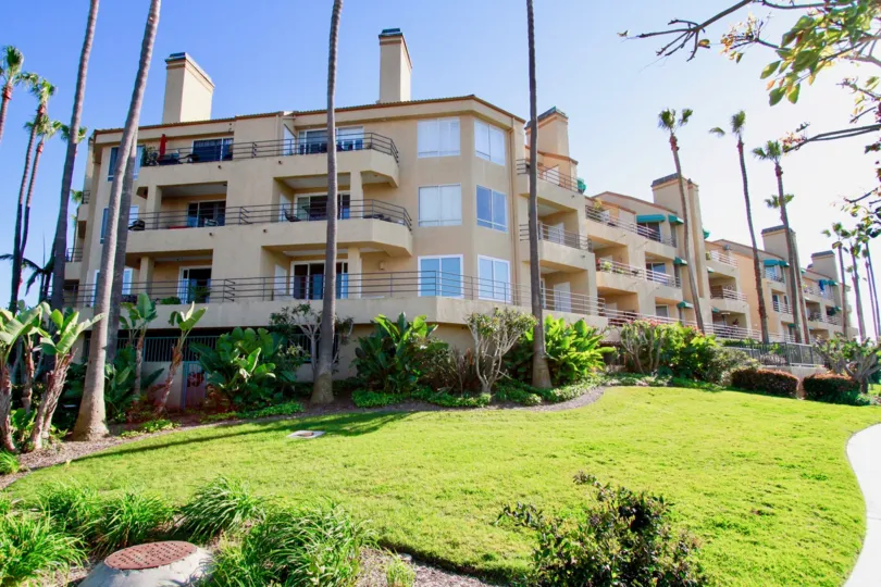 The big apartments in the Portofino Cove with tall palm trees, green grass and flowering plants.