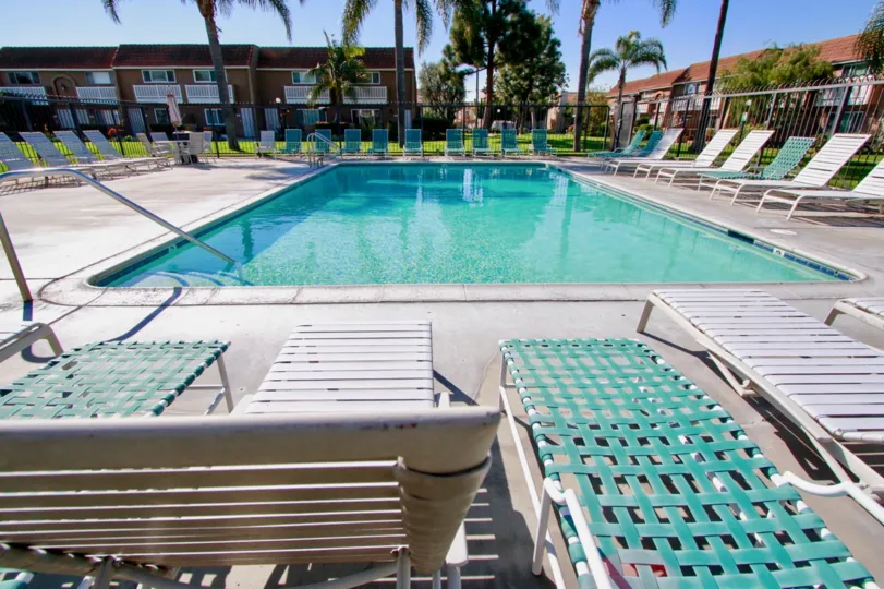 A sunny day in the riviera Huntington with swimming pool, trees, chairs, tables, lawn, and also with beautiful homes.