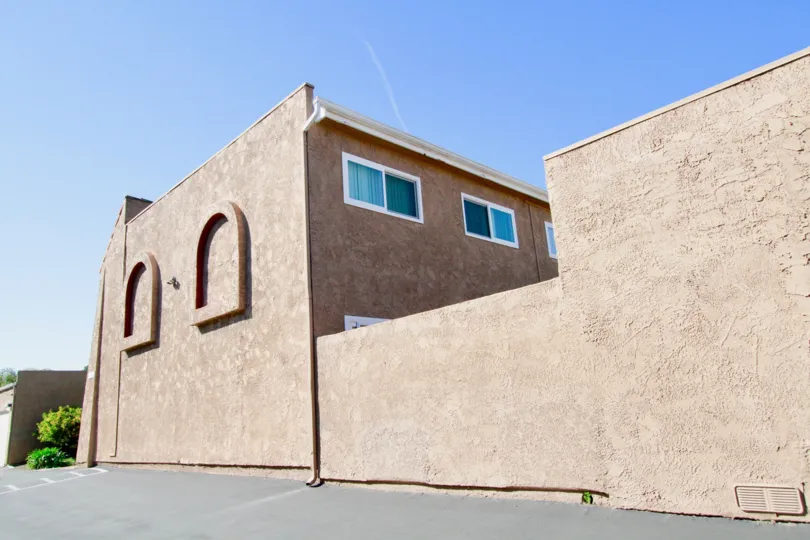 A brown stucco building with a cement parking lot.