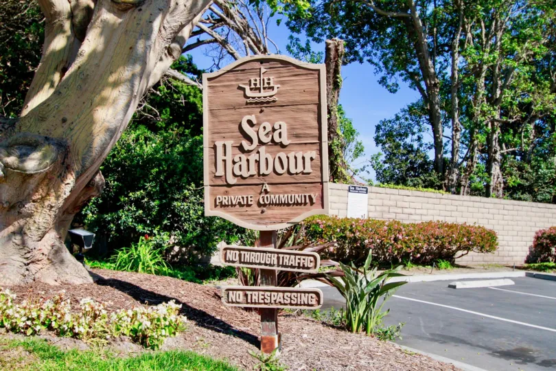Entrance sign that is tan in color with lots of trees behind in the Sea Harbour community.