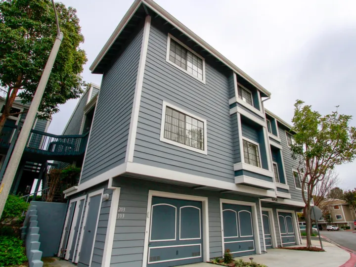 The blue Seabridge Townhomes with bright green tree landscaping and a cement sidewalk entrance.