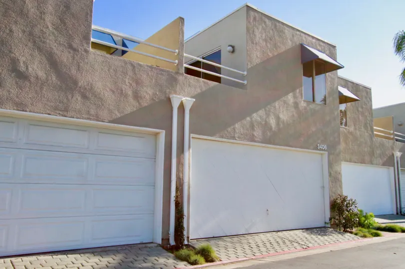 The buildings with big white doors in the Seabridge with glass windows and shrubs near the road side.