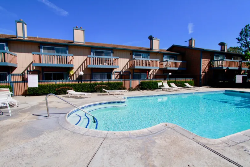 THE BUILDING WITH A SWIMMING POOL AND SUN SHINE AT THE POOL SOME SITTING CHAIRS ALSO NEAR TO THE POOL.
