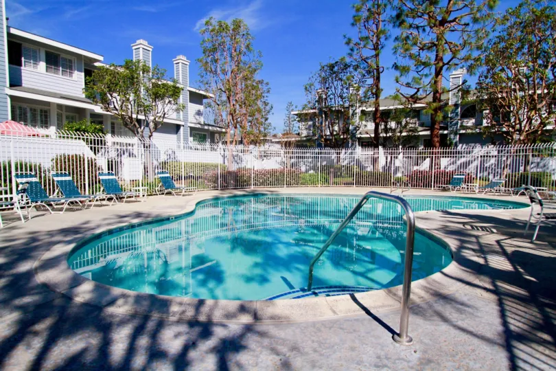 A sunny day in Seawind Cove with swimming pool, chairs, fencing, trees and plants.