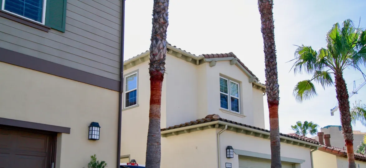 The Waterfront homes with palm trees and garage on a sunny day.