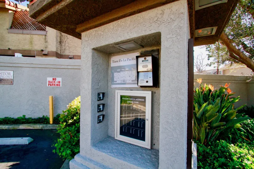A CALLING BOX LOCATED AT A WALL AND A BOARD NEXT OF WALL CONTAIN NO PARKING AND ALSO A SMALL SIGN NEAR TO THE PLACE AND IT LOOKS LIKE A HOUSE WAY.