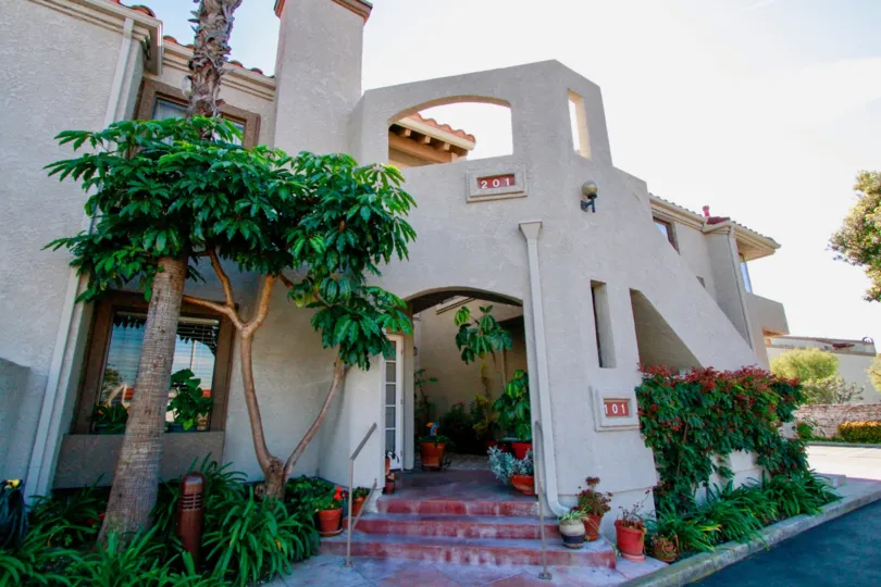 Tiara De La Pacifica two story apartments with trees and bushes on a sunny day.