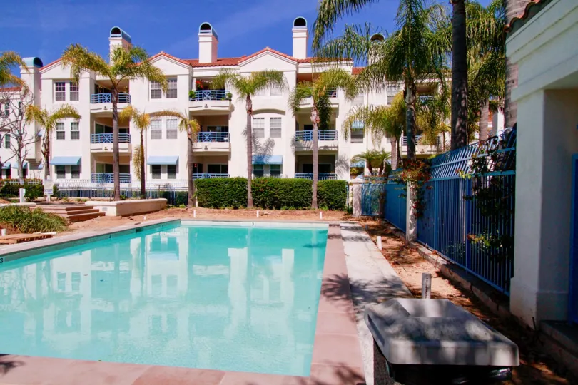 Townsquare Condos pool with a fence and bushes on a sunny day.
