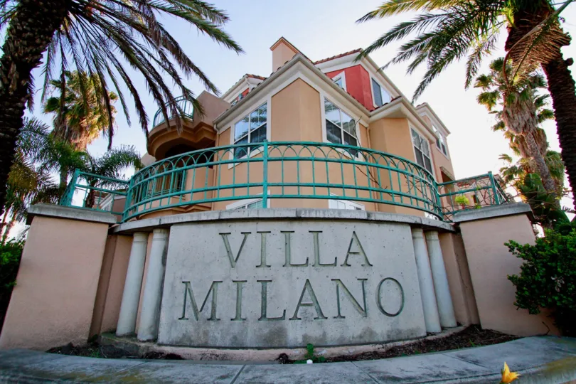 Villa Milano sign with palm trees on either side on a sunny day.