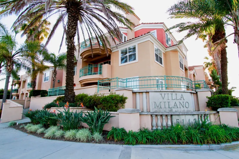 A residential building tan and light pink in color with the entrance sign to Villa Milano community/