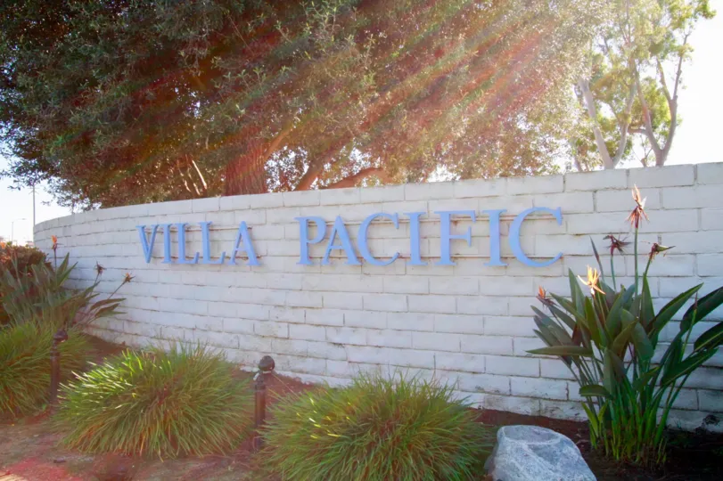 Villa Pacifica stone sign with bushes and trees on a sunny day.